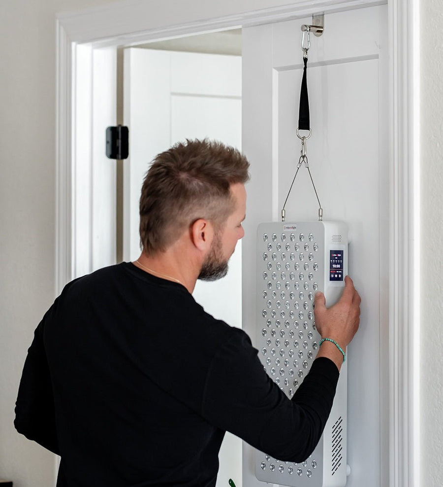 Person adjusting a MitoPRO X red light therapy panel hanging from a door