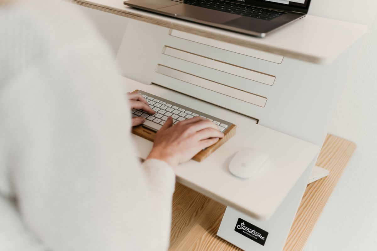 Person typing at an ergonomic adjustable desk with a computer monitor