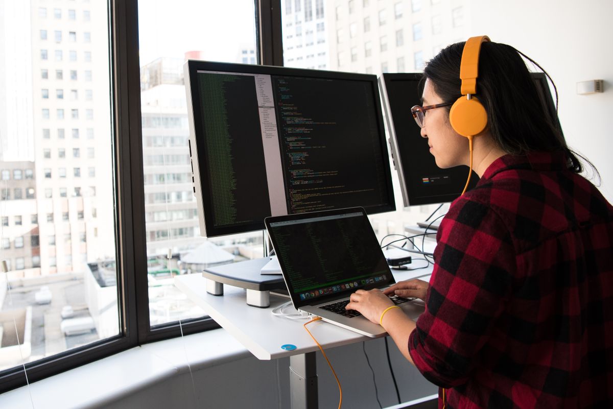 Person working at a standing desk with computer screens in an office